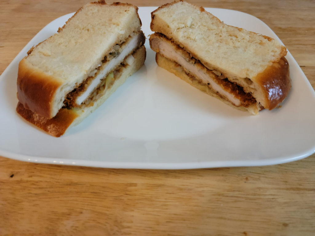 A pork katsu sandwich cut clean into two rectangles on a square plate.