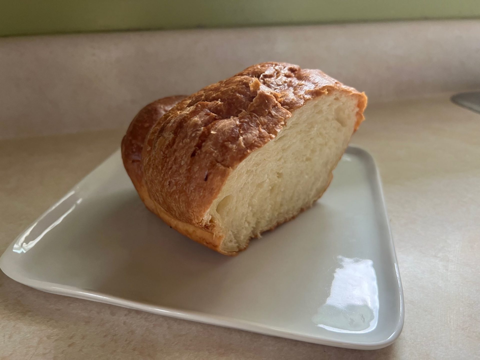 A half loaf of bread made from croissant dough, sitting on a square white plated on a light colored countertop.