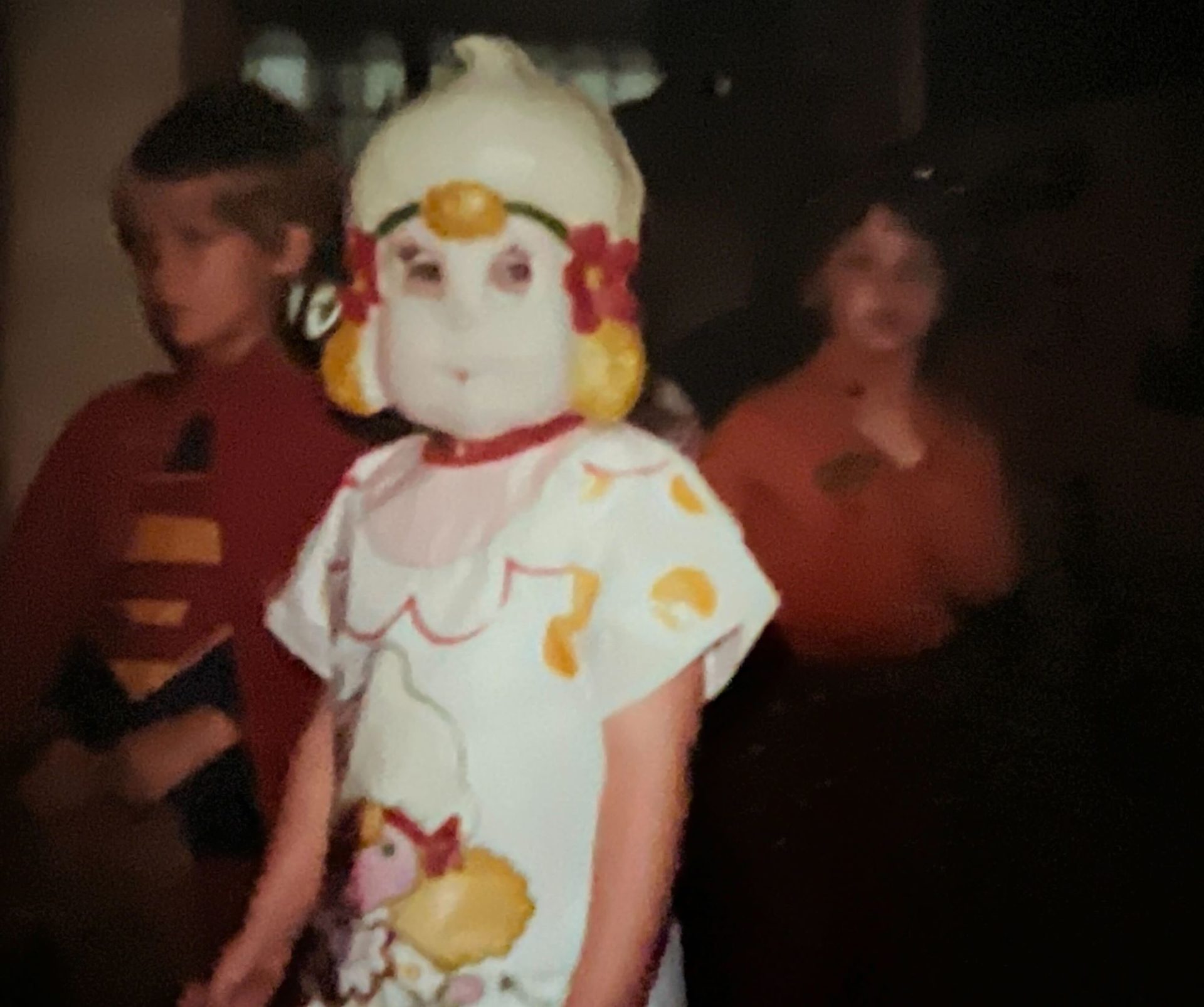 A young child dressed in a plastic Halloween dress and plastic Lemon Merengue mask.