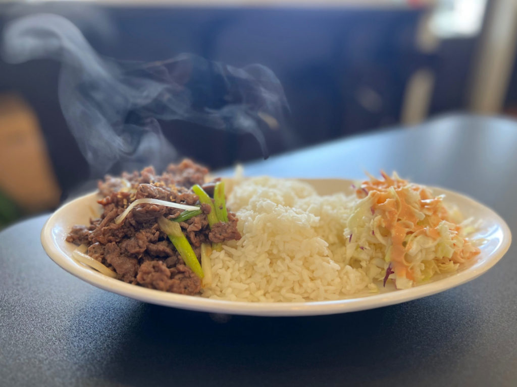 A white plate with beef bulgogi, white rice, and a simple salad with an orange dressing on a black table at San Maru in Champaign.