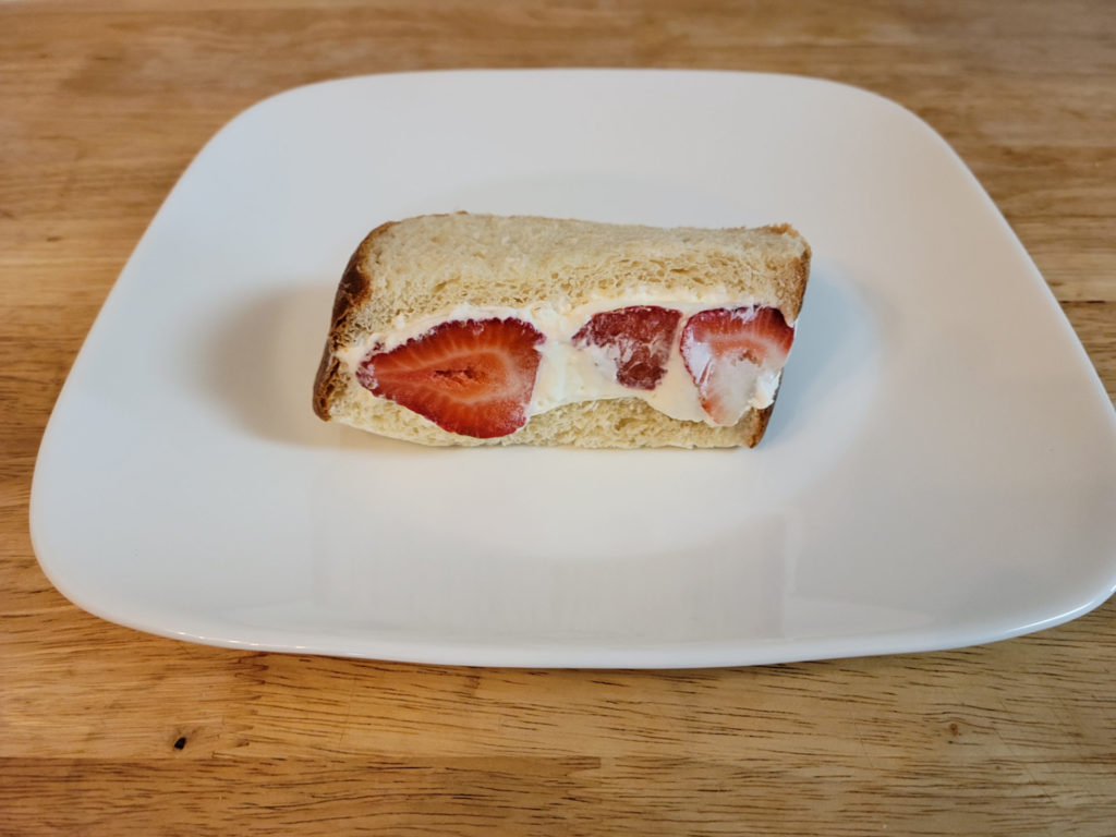 A strawberry fruit sandwich that is half the size of the pork katsu sandwich on a square plate.