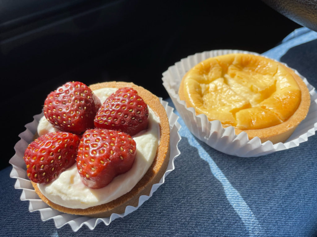 On the left is a strawberry tart. There are four heart shaped strawberries laid on the circular crust. On the right is a maple cheesecake tart. It has a round crust and a pale yellow center.