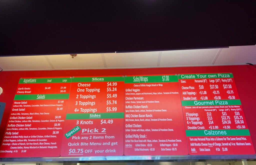 A red menu with white font listing appetizers, salads, slices of pizza, sides, subs, wraps, calzones, and pizza.