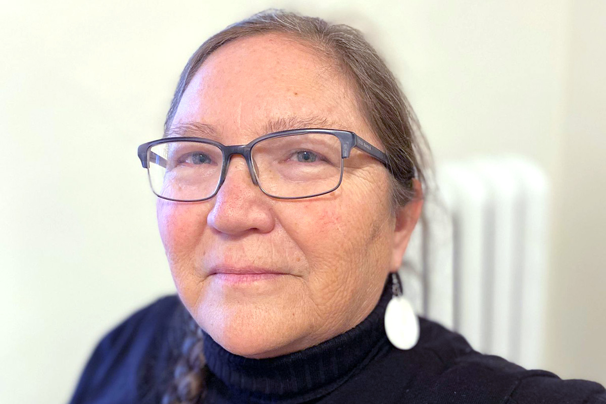 A Native American woman with glasses and hair that is pulled back. She has silver earrings and a black top.