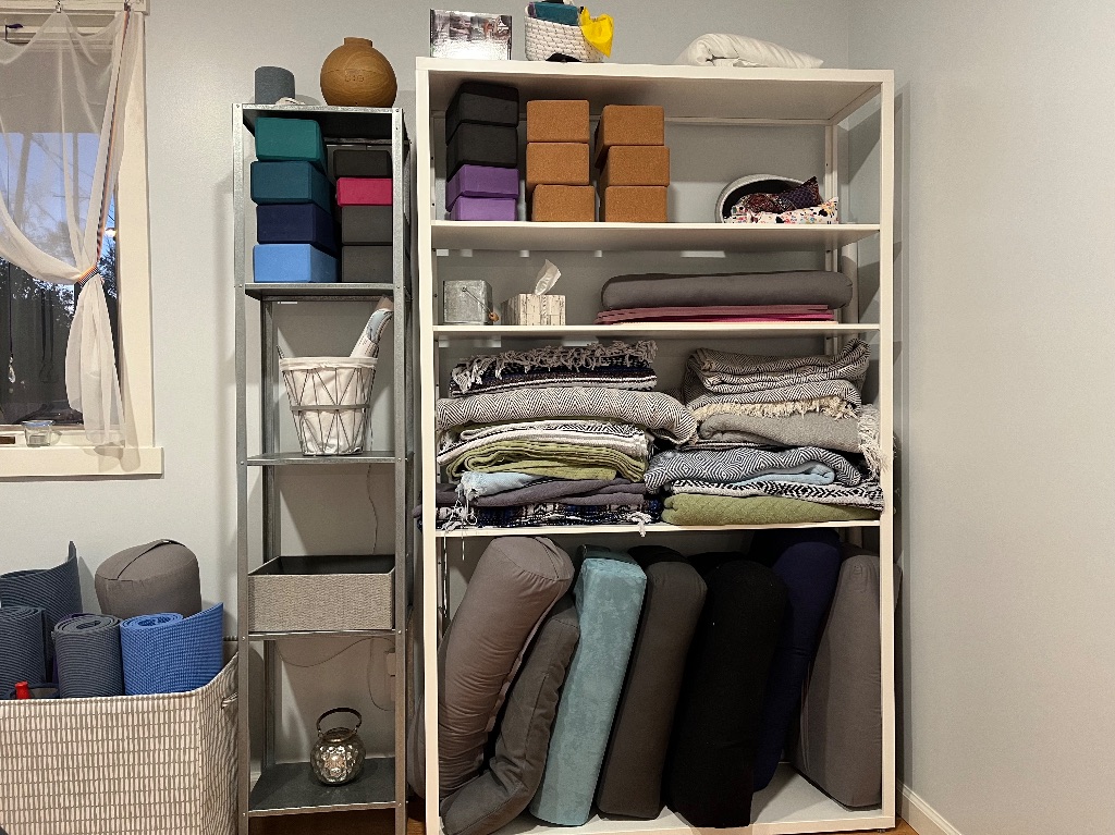 Against the wall there is a big shelf full of yoga mats, blocks, and blankets folded and stacked.