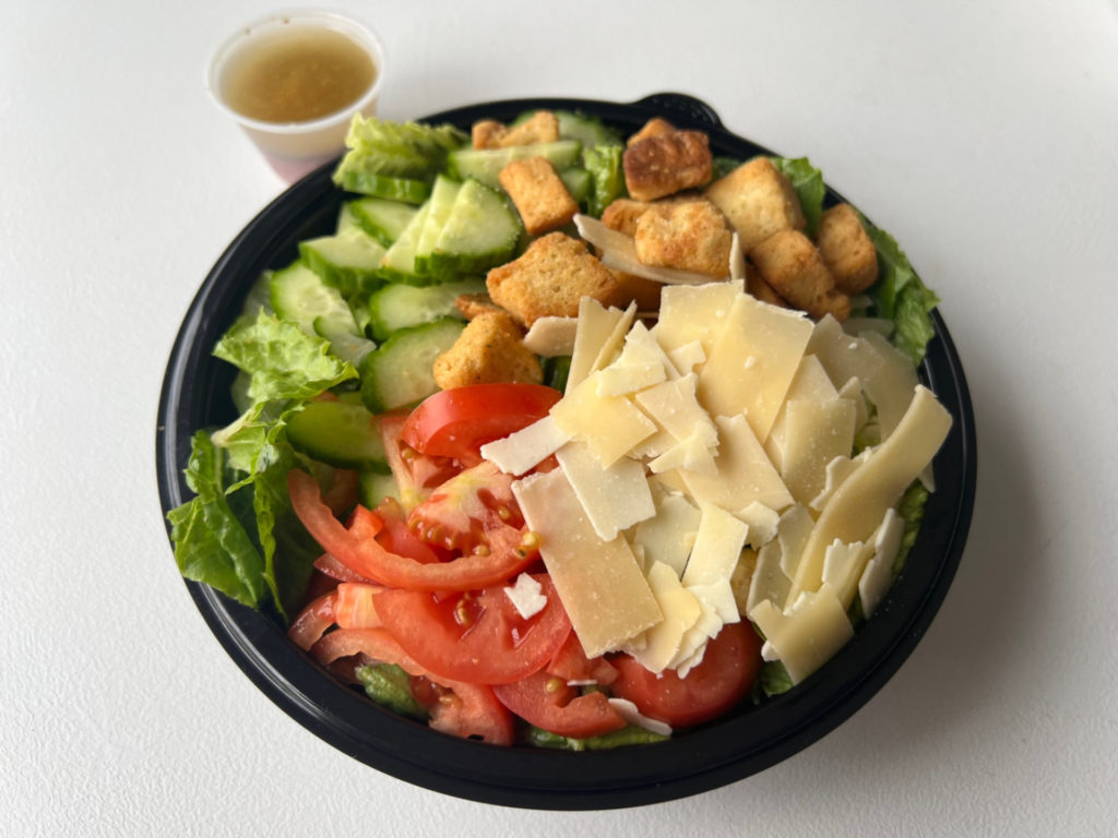 A salad from DP Dough has shaved parm, sliced tomatoes, cucumbers, croutons, and romaine.