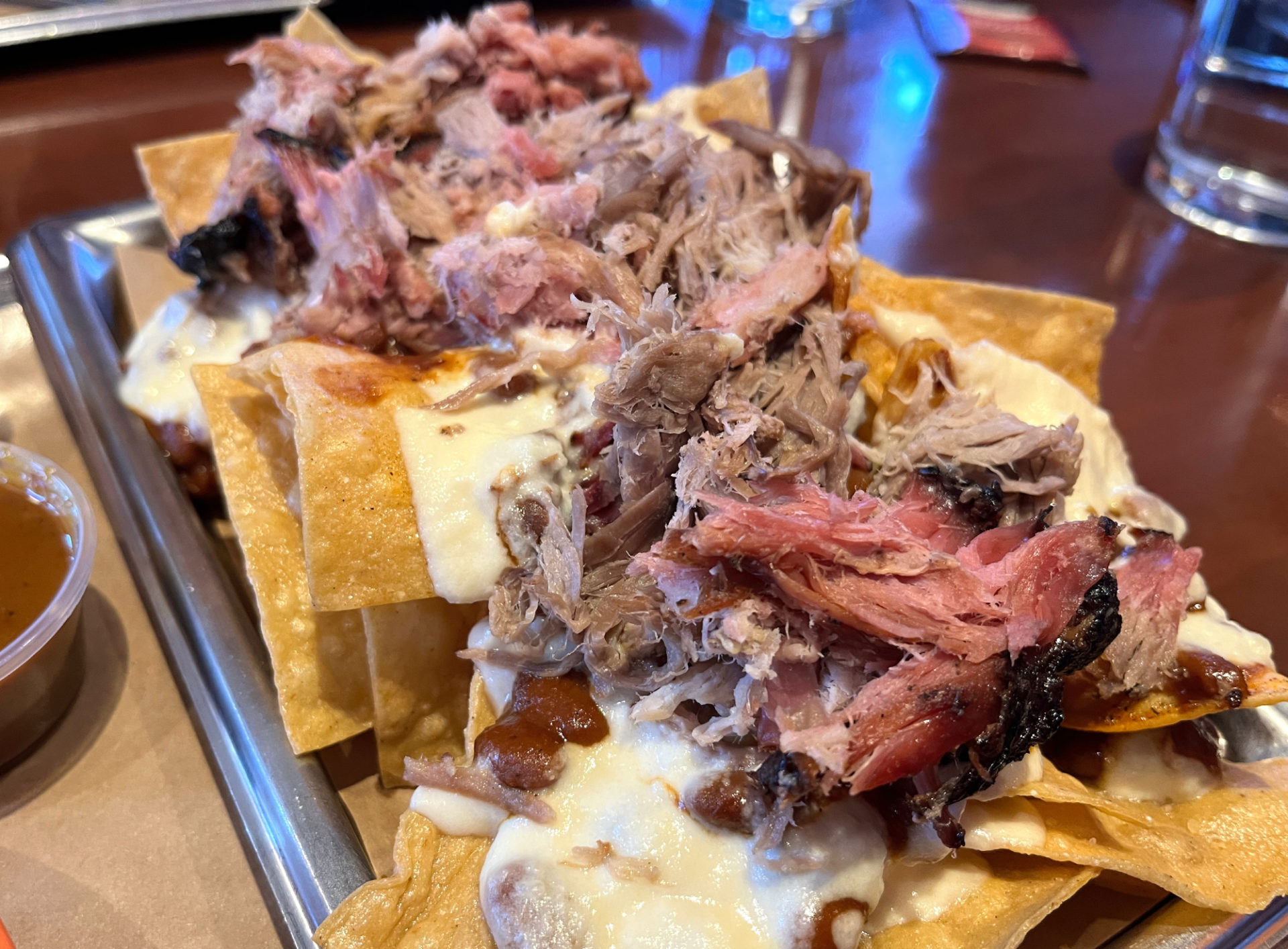 A plate of pulled pork nachos at Black Dog. Golden chips are piled with white cheese and pulled pork on a rectangular silver tray.