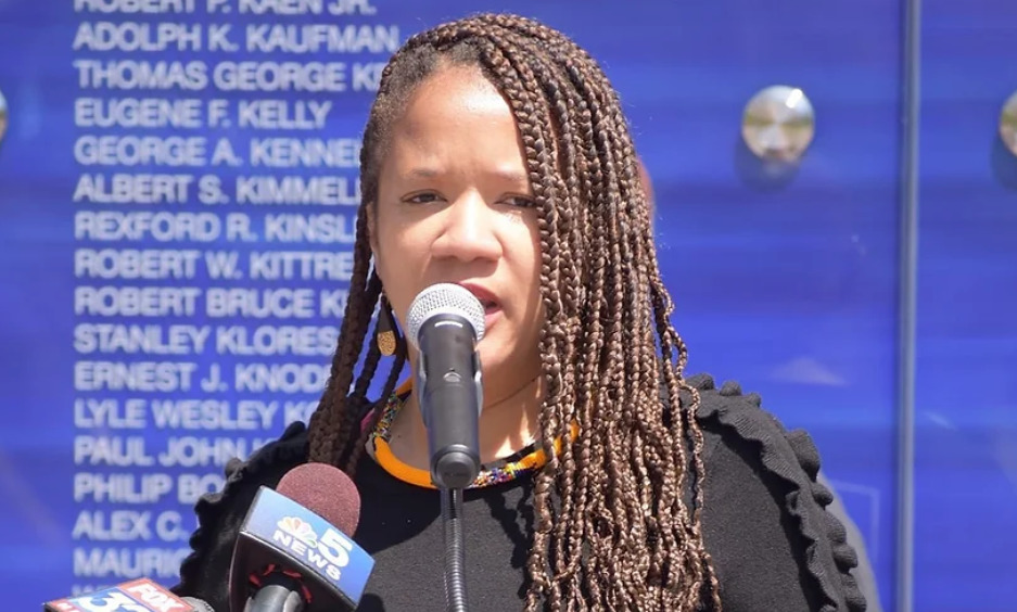 A Black woman with long braids is speaking into a microphone.