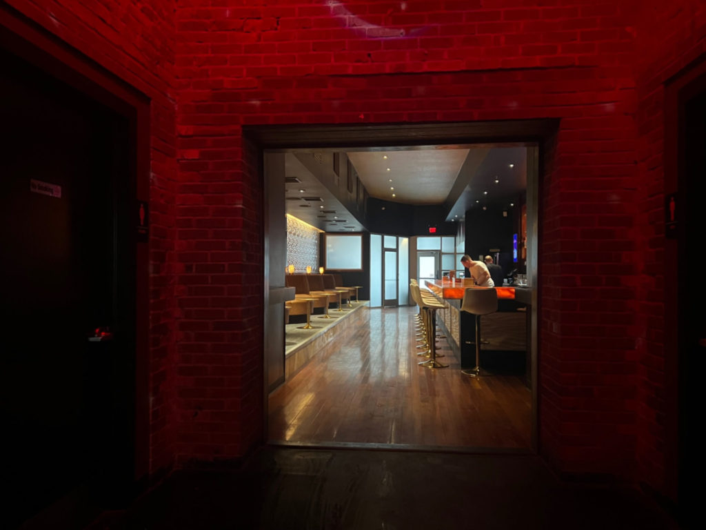 A brick room with red lighting that has a view of the front lounge.