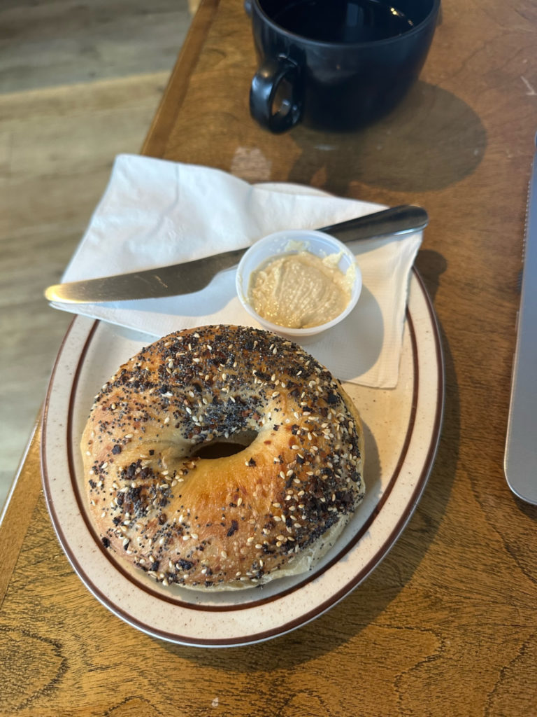 An everything bagel with a side of hummus on a wooden table.