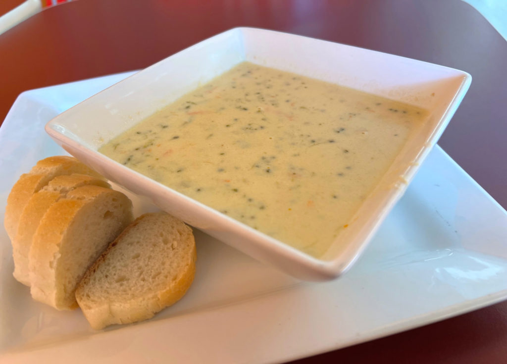 Broccoli cheddar soup in a square bowl with four slices of white baguette on a white plate at Rick's Bakery in Urbana, Illinois.
