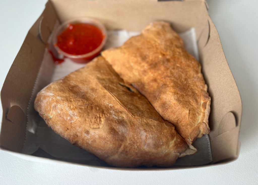 A full sliced calzone in a to-go box.
