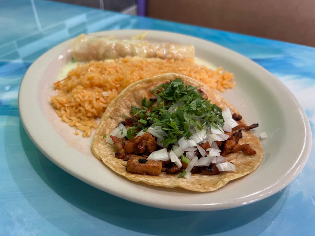An al pastor taco on a white plate with Mexican rice and a cheesy enchilada.