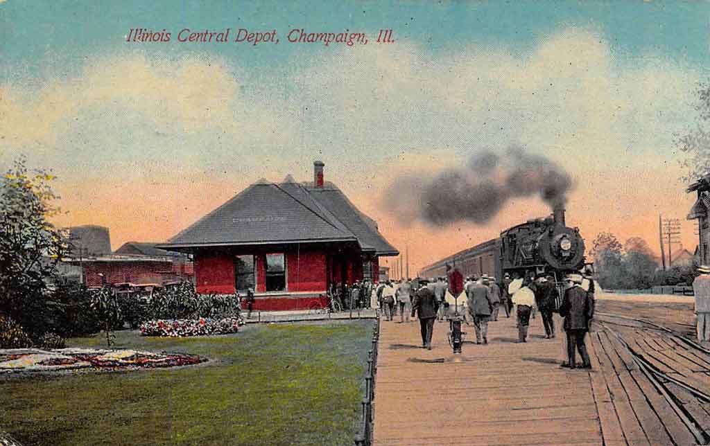 A illustrated color photograph of the Illinois central depot a red one story building on the left and on the right a platform with people walking on it and a large locomotive with billowing black smoke.