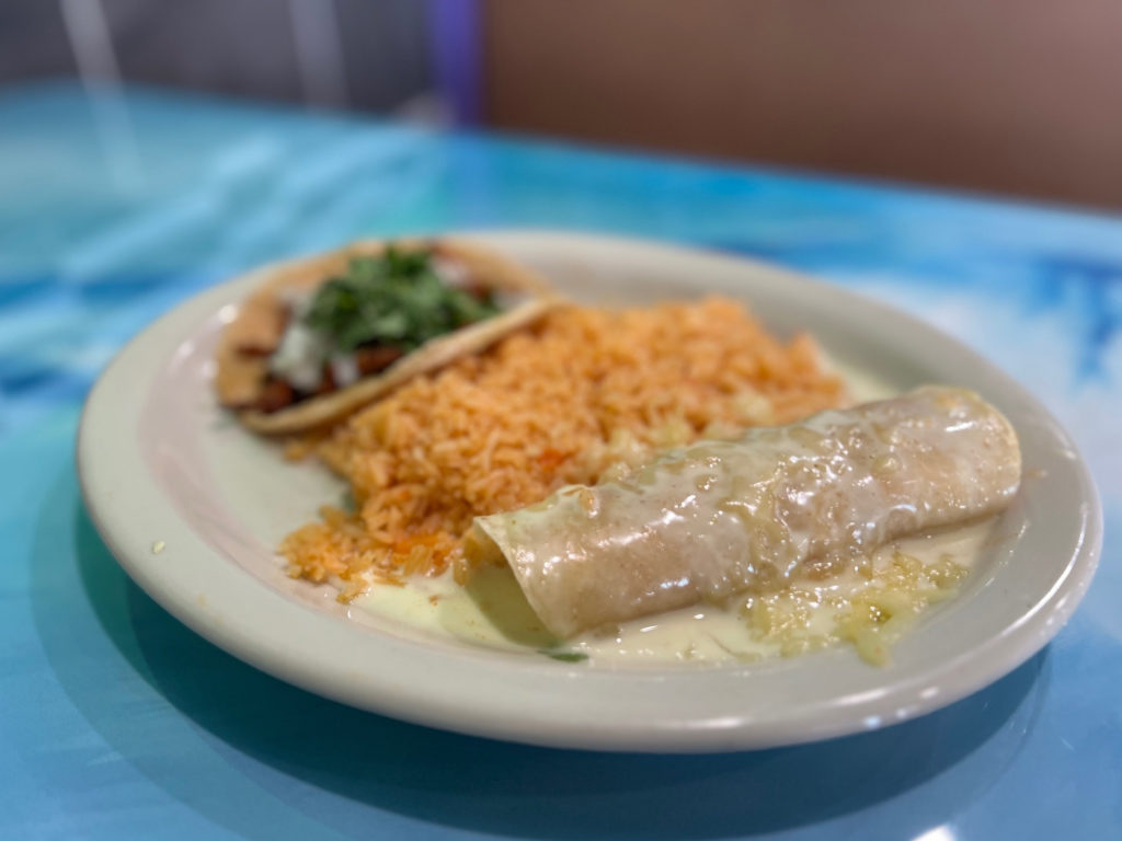 A cheesy enchilada on a white plate with Mexican rice and a taco.