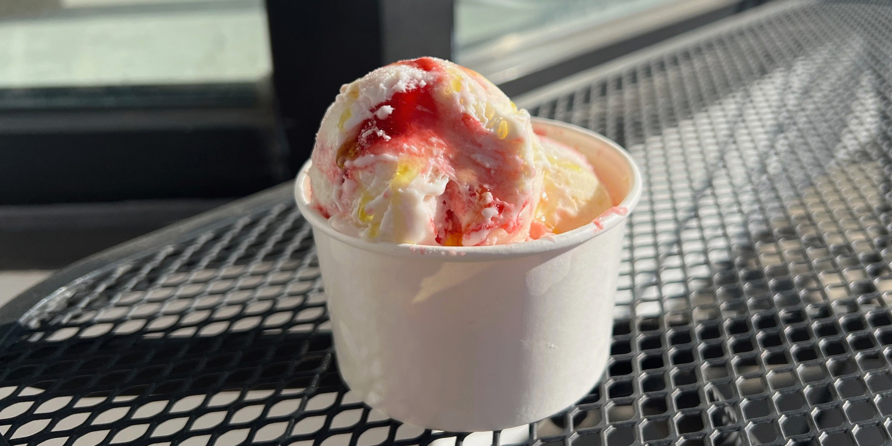 A cup of strawberry cheesecake ice cream with olive oil on top on a patio table outside of Grovestone in Champaign, Illinois.