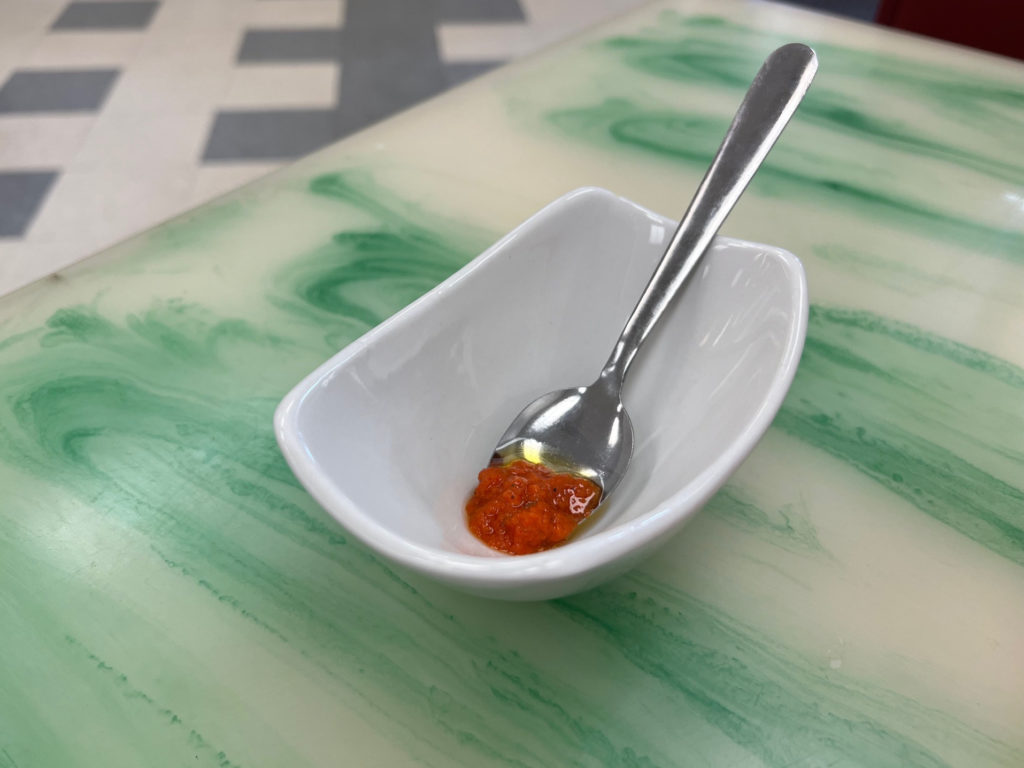 A white bowl with a spoonful of red pepper sauce.