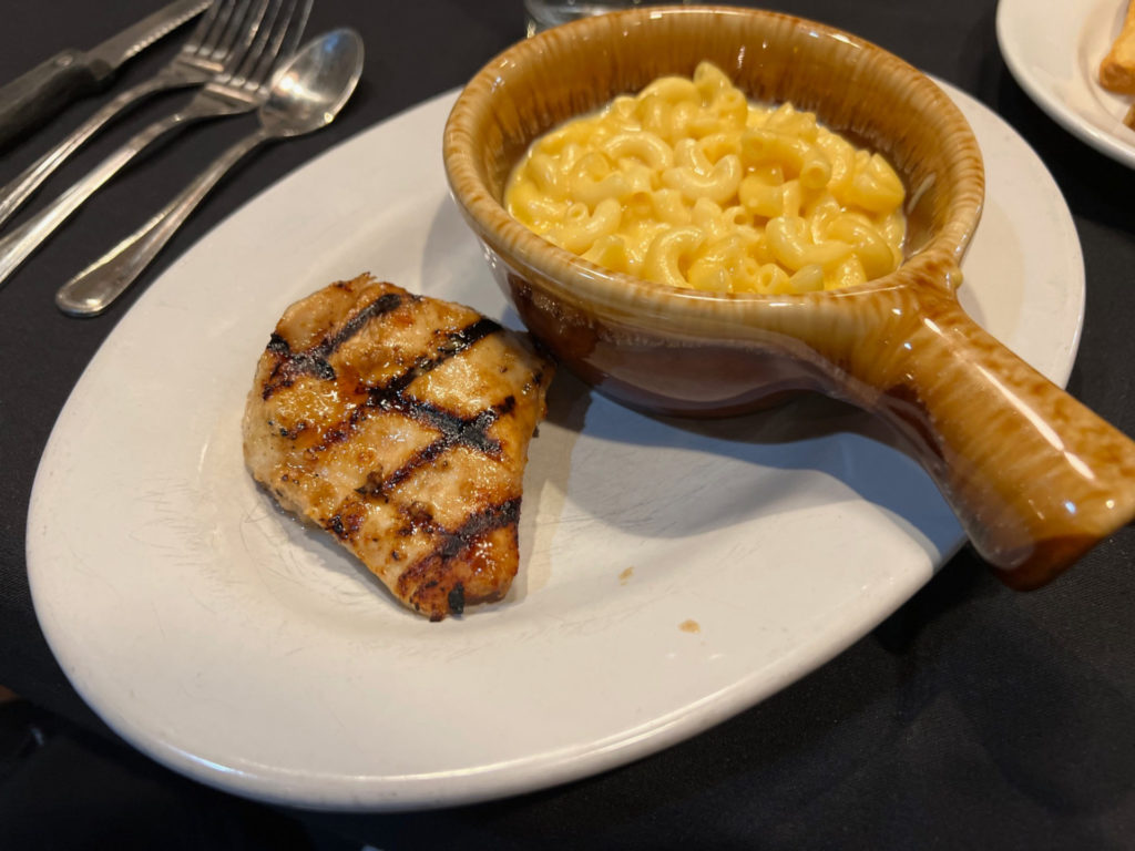 A small piece of chicken beside a bowl of macaroni.