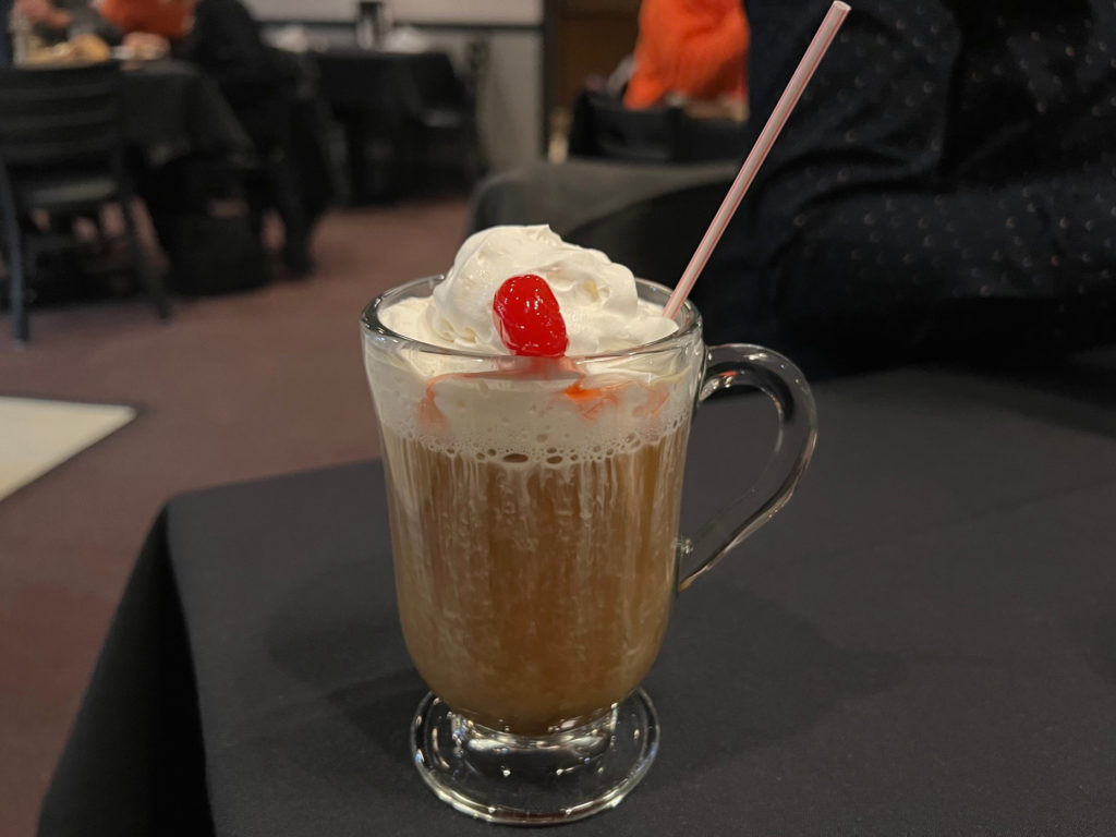 Coffee cocktail in a cup with whipped cream and cherries.