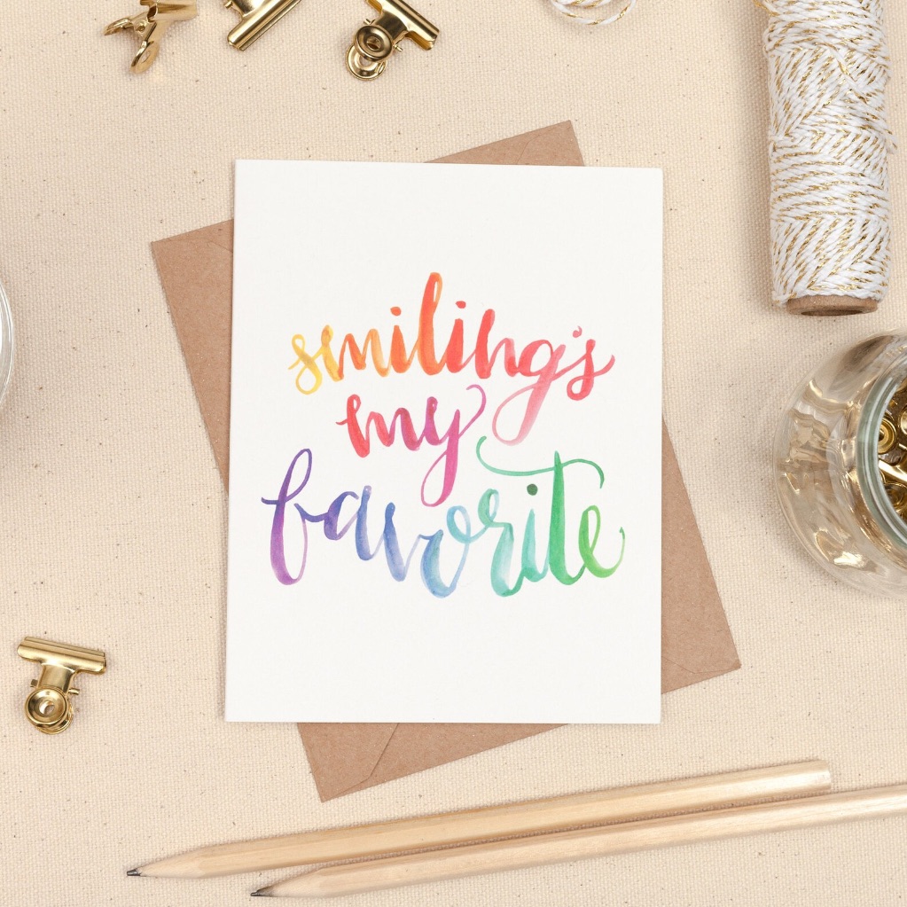 A card on a desk surrounded by pencils, string, and gold clips. The card says "smiling my favorite"