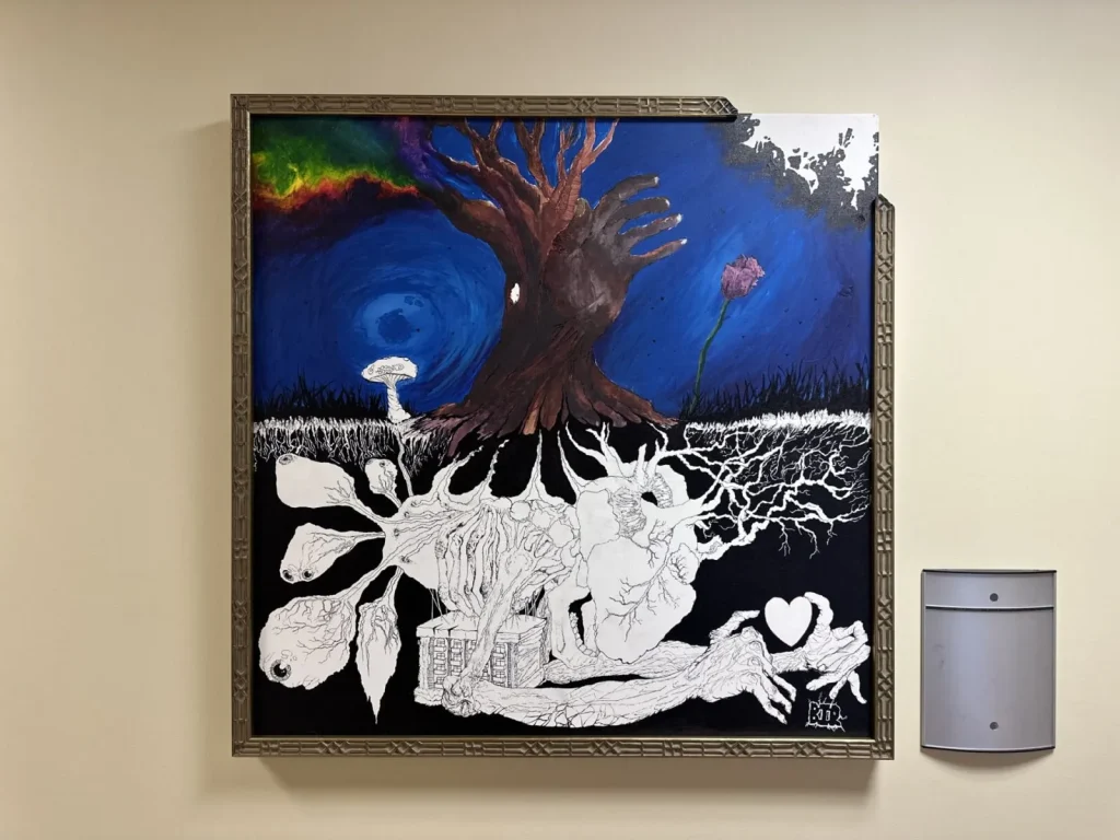 A painting of a tree against a deep blue background. The bottom half shows in black and white the "roots" which appear to be a human heart, and hands along with eyeballs. The top right corner of the frame and painting are missing. 