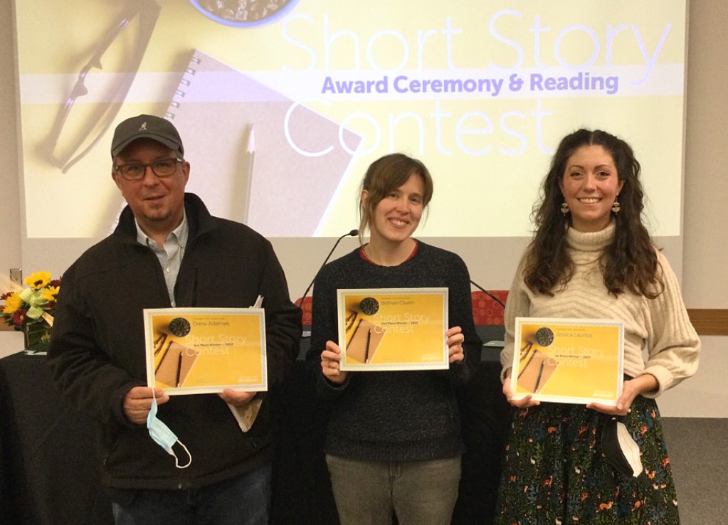The Three people who won the short story contest in 2022 stand next to each other holding yellow certificates. 