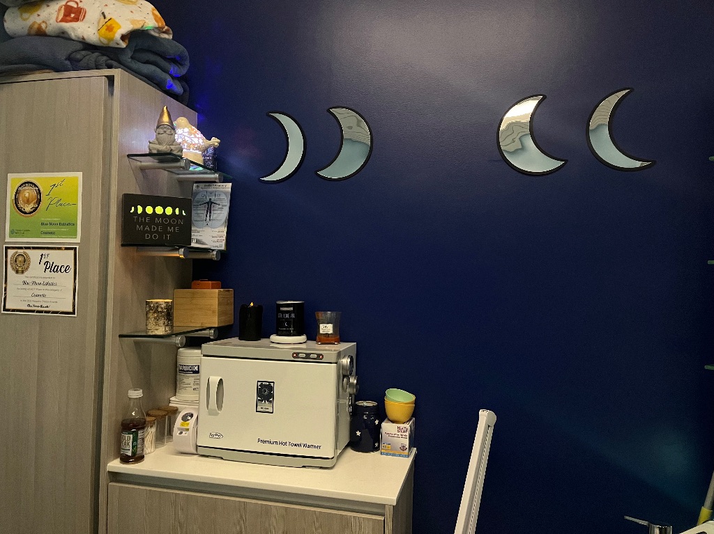 A dark blue wall with mirrored moons in different phases. underneath is a small counter and shelves with various products. 