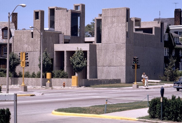 A gray building made up of varying sizes of rectangular sections, situated on an intersection.