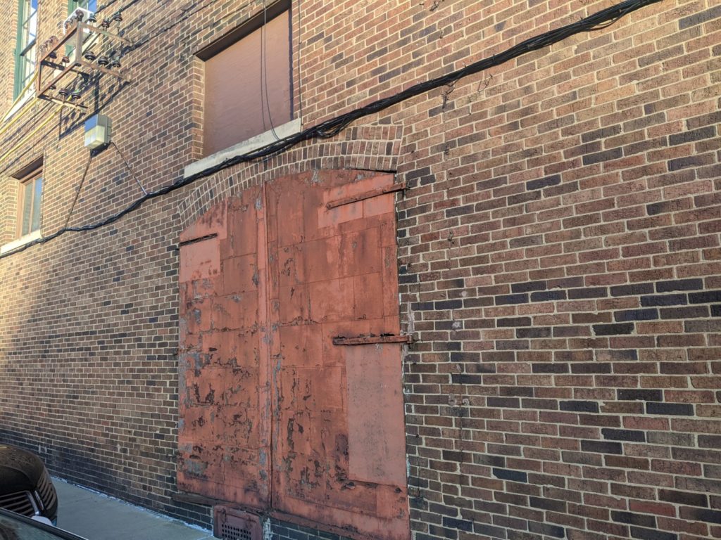 A giant distressed wooden double  door attached to a brick building. 