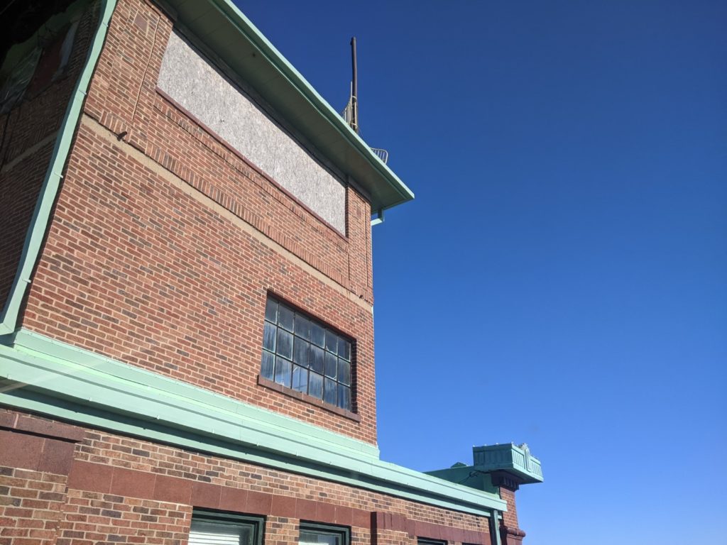 The observatory floor on the Lincoln building. It is outlined in green copper and the rest of the building is brick set against a blue cloudless sky. 