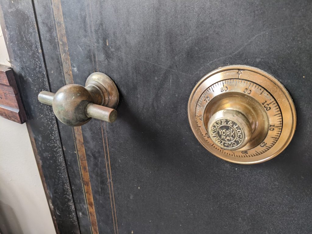 A close up view of a black safe door. The dial is shiny gold colored  brass and the numbers are visible around the dial. 