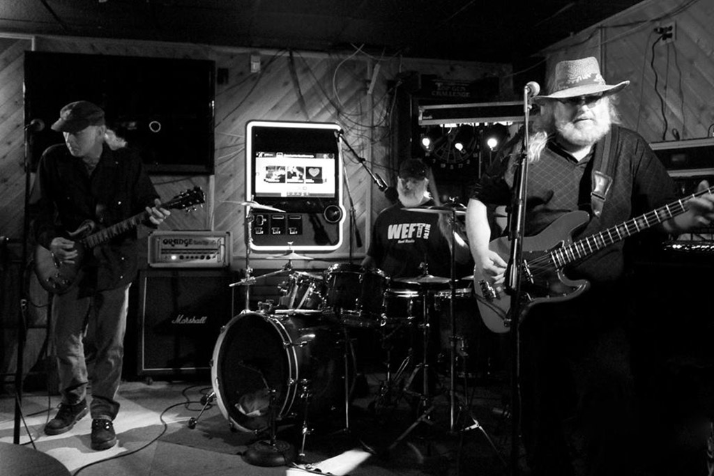 Black and white photo of a 3 piece blues band playing in a studio.