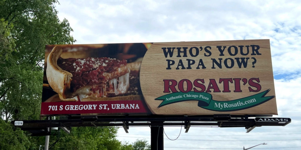 A billboard advertising Rosati's pizza. On the left, a slice of deep dish pizza. On the right, text that reads "Who's your papa now? Rosati's authentic Chicago Pizza MyRosatis.com."