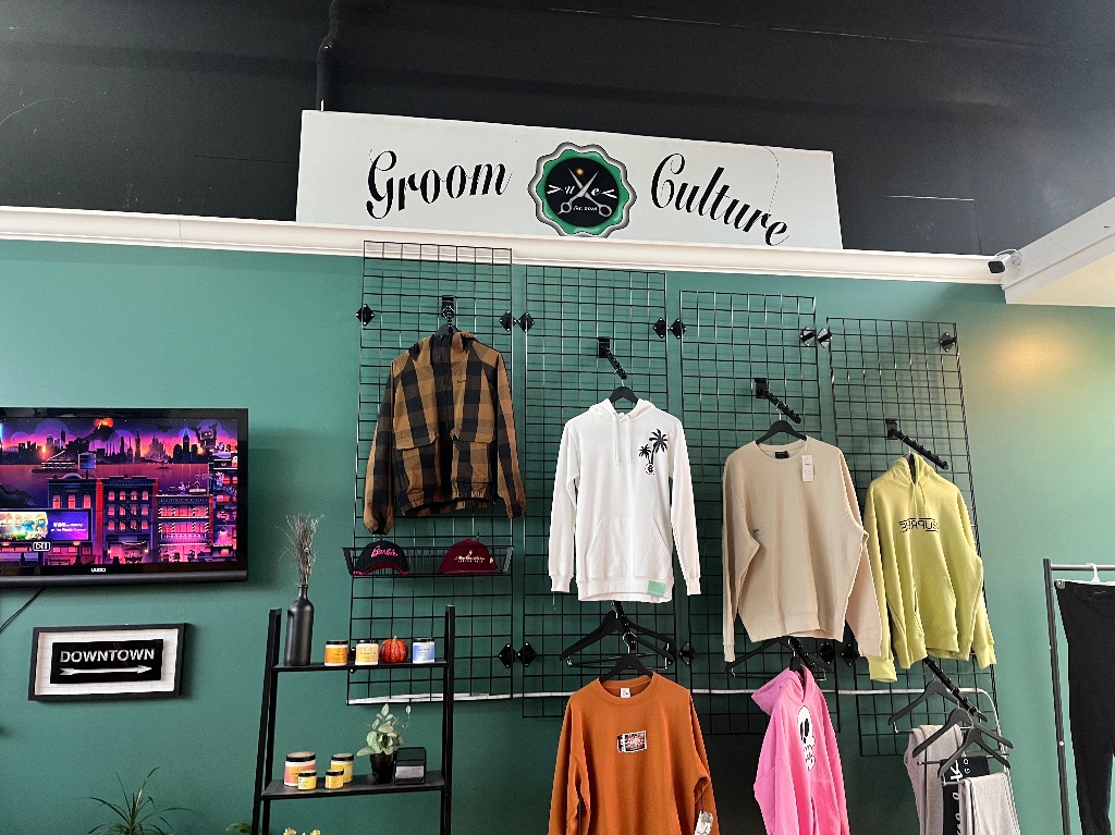 The inside of groom culture. A green and black wall with multiple long sleeve shirts hanging up.