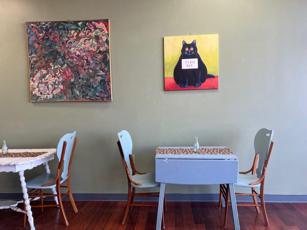 Inside Lucky Moon Bakery in Mahomet, there are painted tables with art above it. One is a black cat with a sign reading "Feed Me."