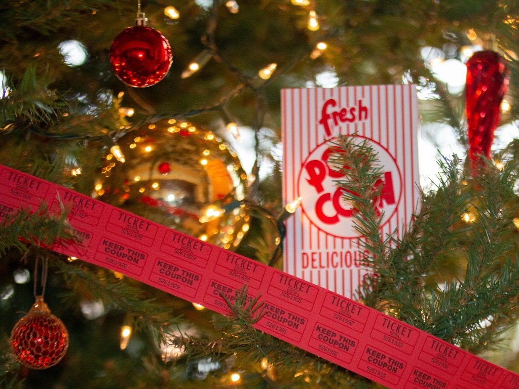 A close up of a tree with red movie tickets and popcorn sitting in the branches with white lights and ornaments decorating the tree.