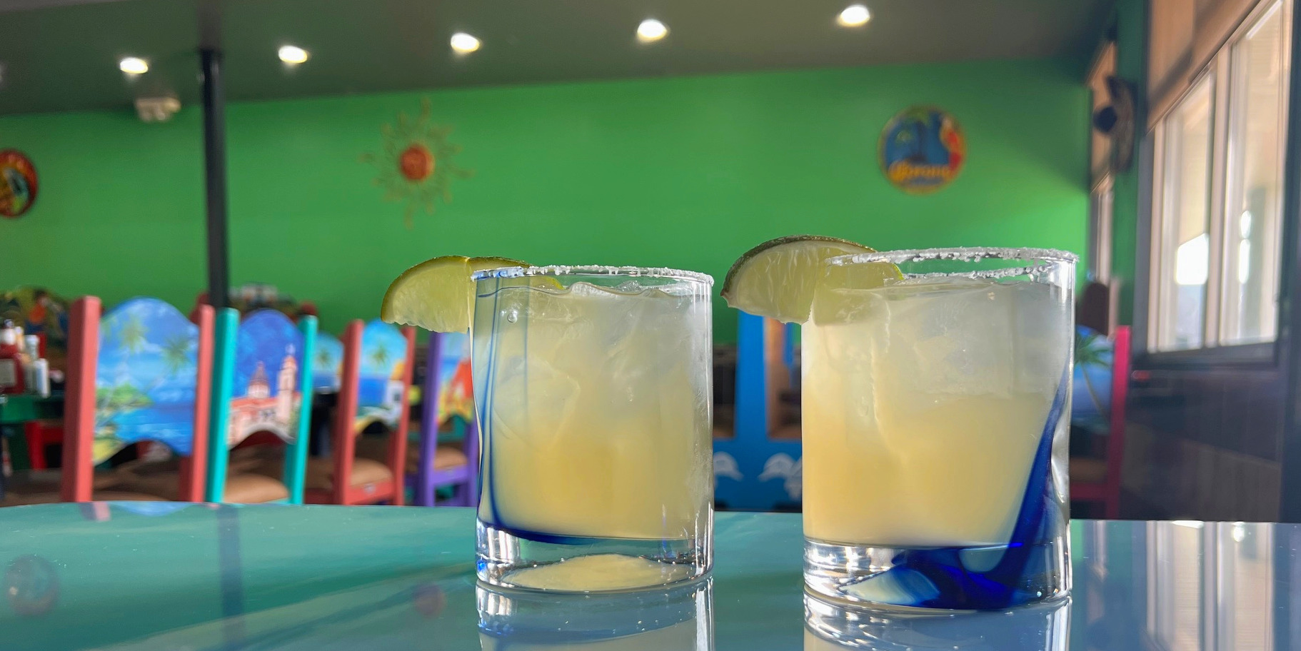 Two margaritas on a table in front of a lime green wall at Casa Margaritas restaurant in Champaign, Illinois.