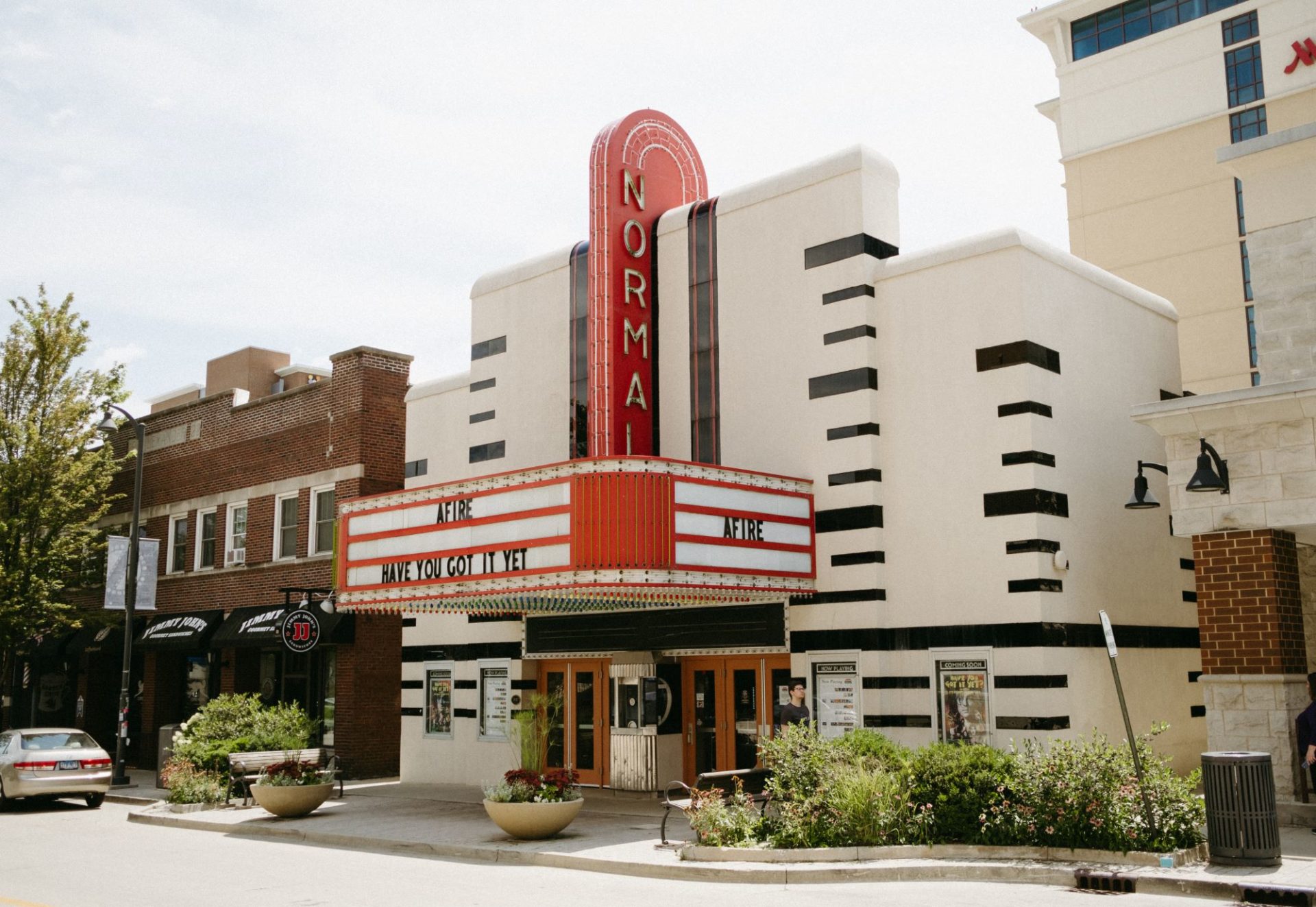 Front of a historic movie theater with a red, curved sign that says Normal in lights. Under the sign is a red and white marquee.