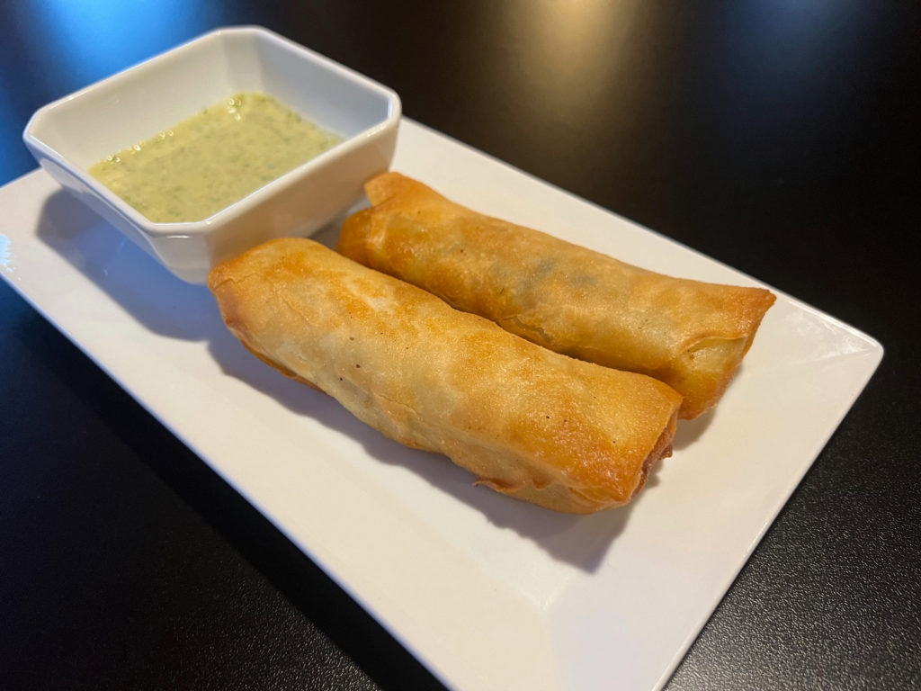 spring rolls on a white plate beside a green chutney at Afghan Cuisine restaurant in Champaign, Illinois.