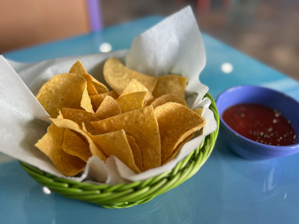 A basket of chips beside a blue bowl of salsa.