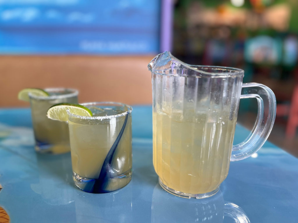 A half pitcher has some margaritas poured into two half glasses with a lime.
