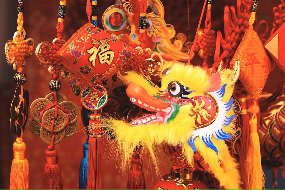 The head of a dragon puppet, with yellow fur, against a backdrop of decorations for Chinese New Year.