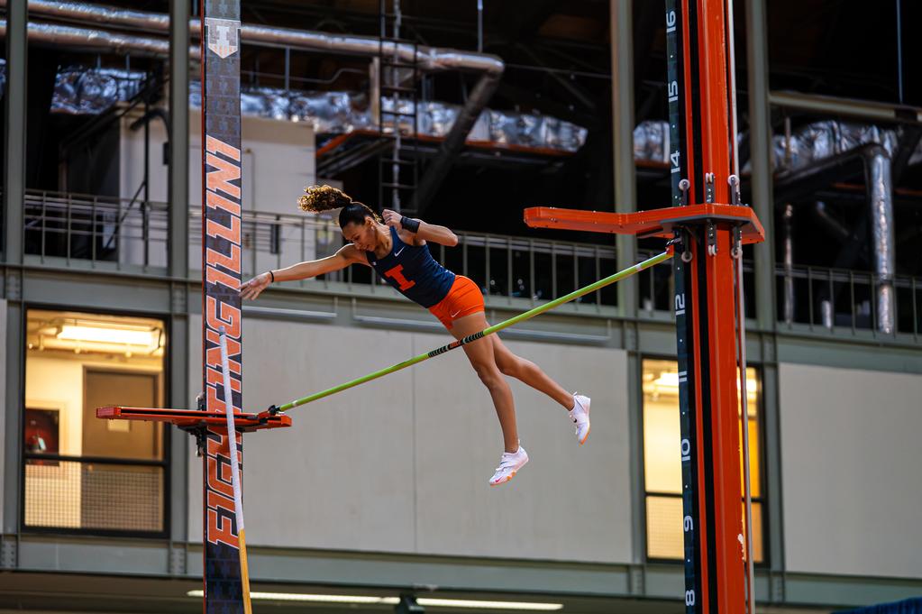 Illinois Pole Vaulter Tori Thomas during the Illini Open at the Illinois Armory in Champaign, IL.She is mid air after vaulting over a bar. She wears a blue jersey with an orange I and orange shorts.