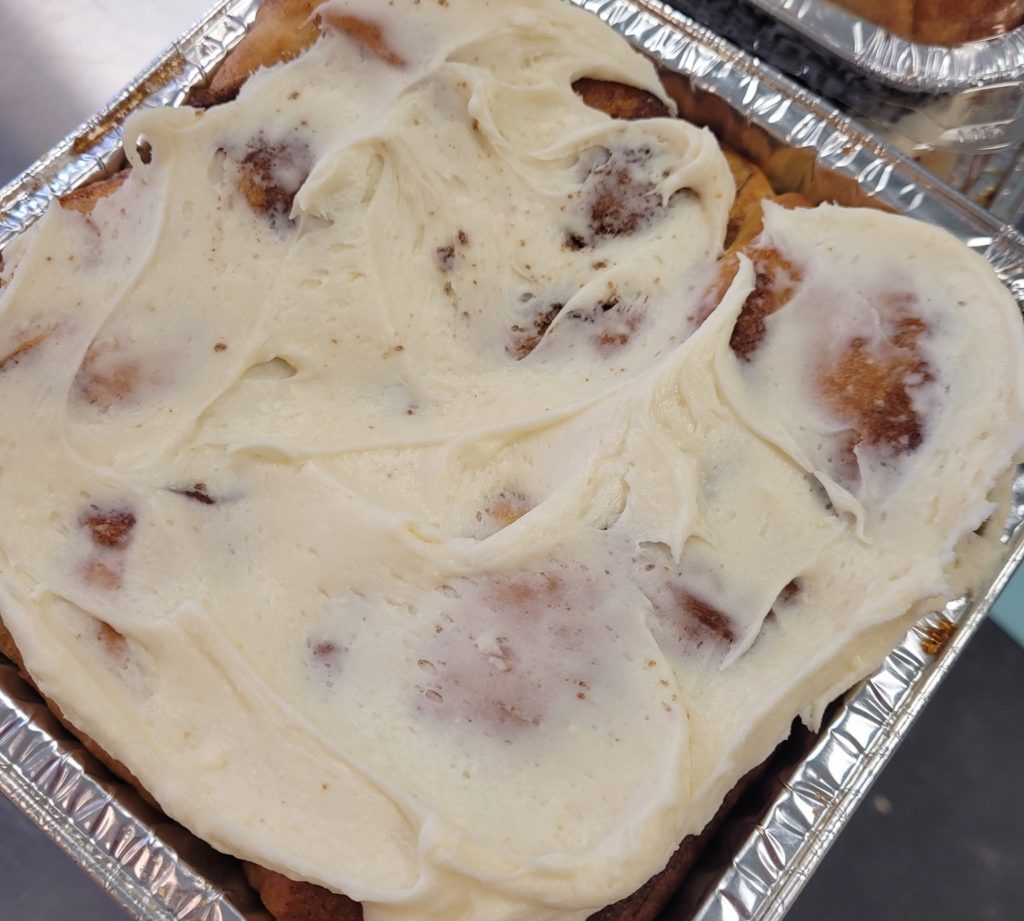 An aluminum tray with cinnamon rolls covered in thick white frosting.