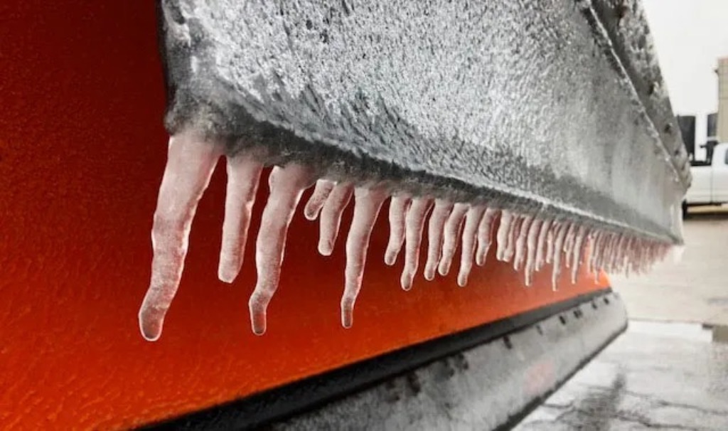 A close up of short Icicles hanging off of a black gutter in front of a red building.