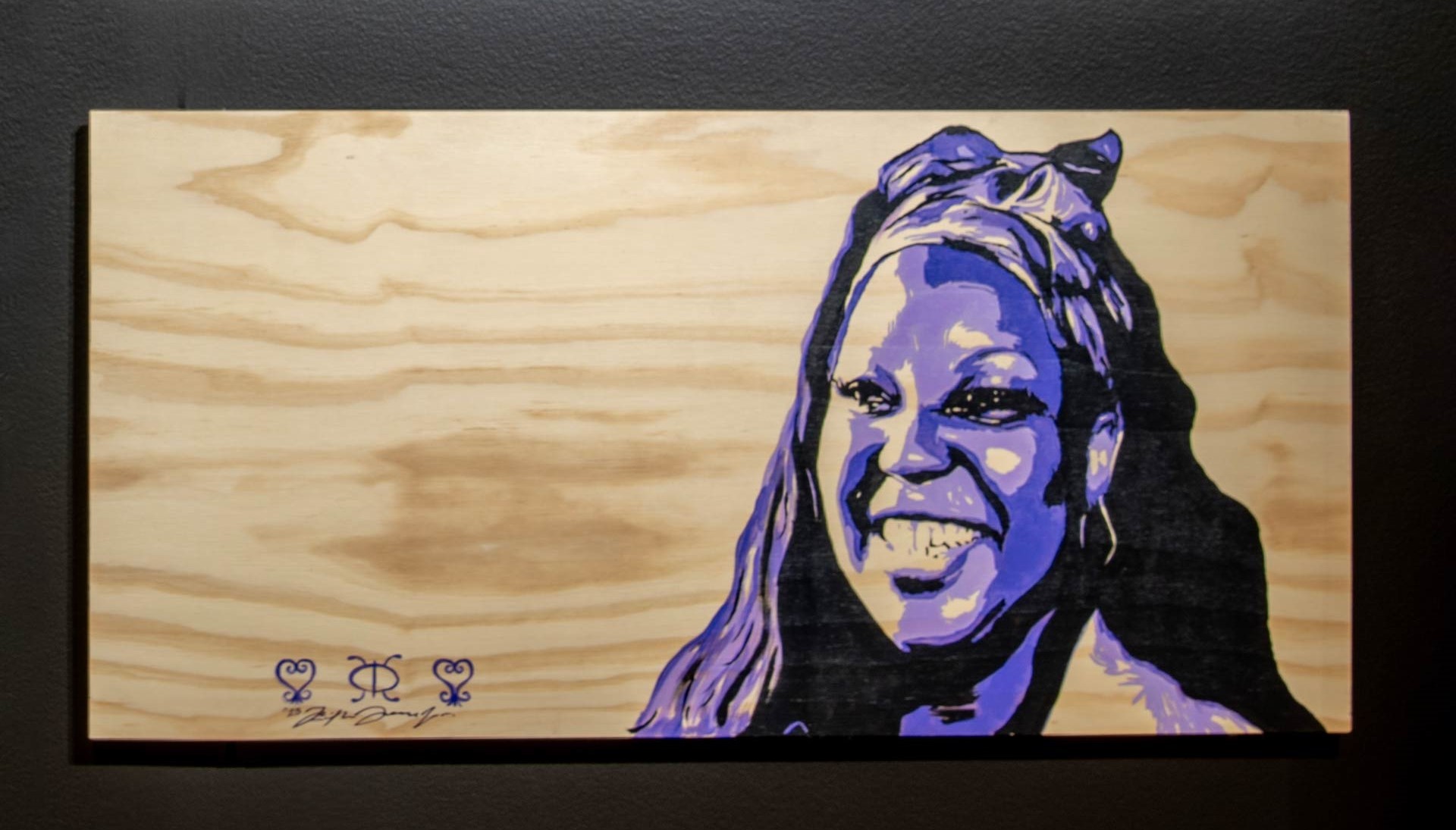 Image of a smiling Black woman with long hair, painted on a wooden plank.