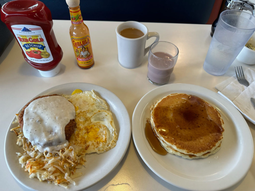 A breakfast order of country-fried steak with eggs, hashrbowns, and pancakes.