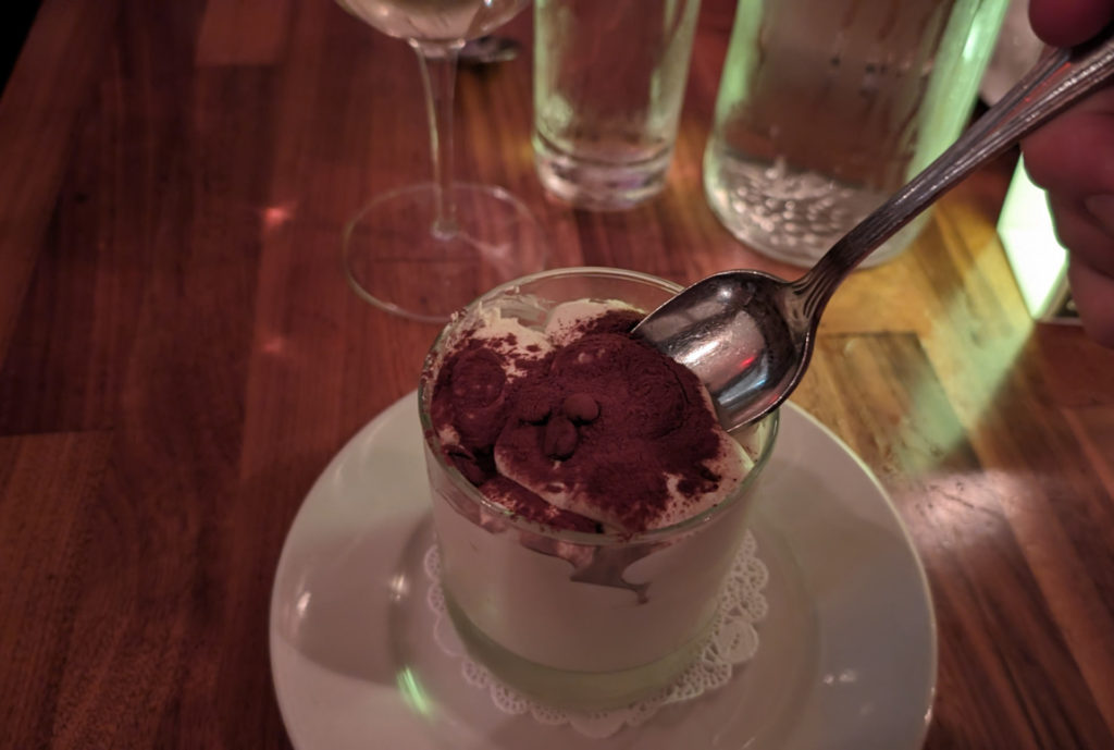 A cup of tiramisu with a silver spoon held by the author.