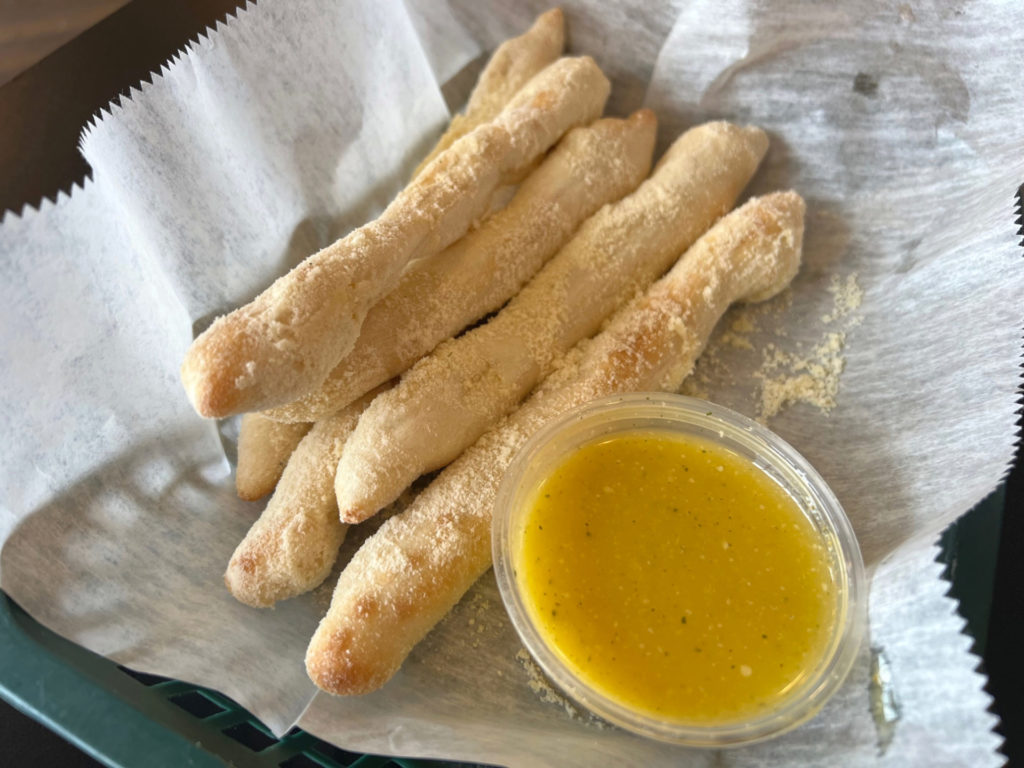 A basket of six breadsticks with a cup of melted herb butter.