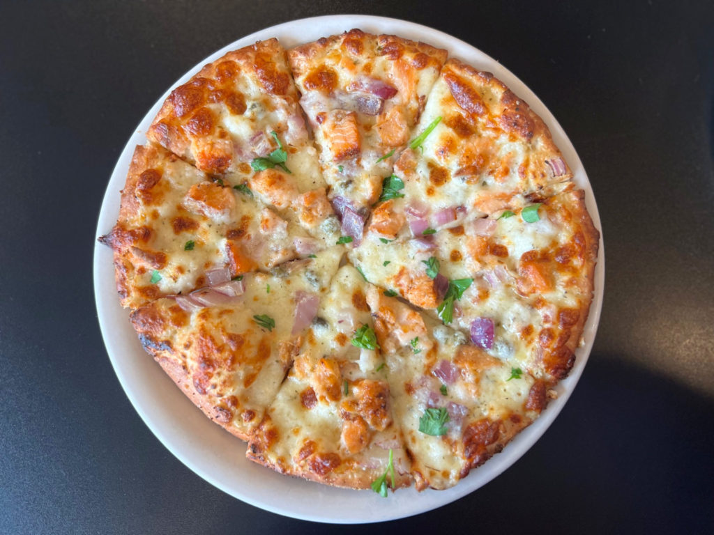 A pizza with smoked salmon, parsley, red onions, and garlic cream sauce.